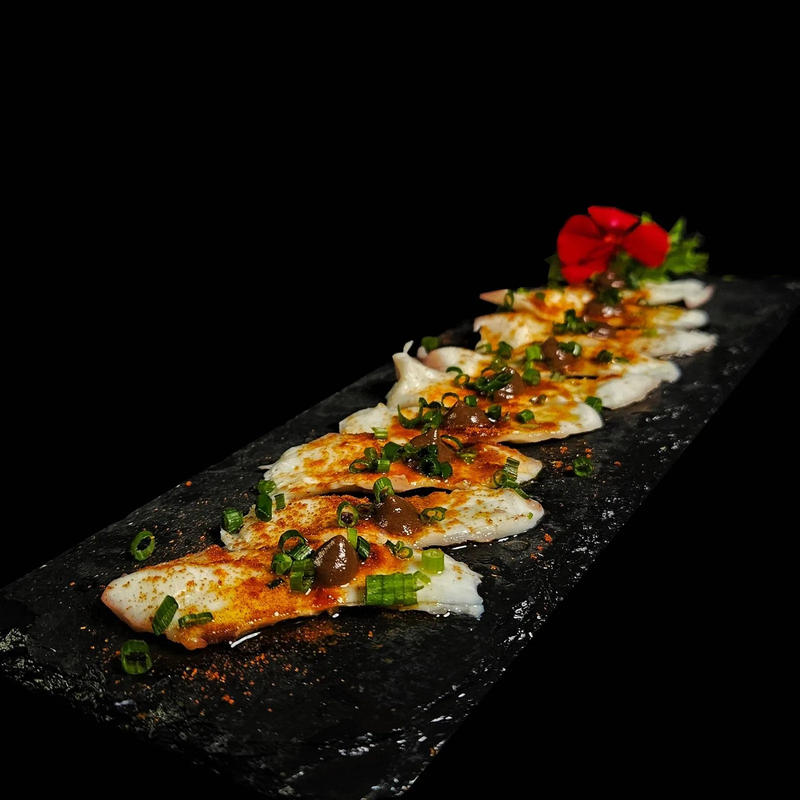 Tiradito de finos cortes de pulpo con salsa de olivas negras, pimentón dulce y ciboulette.